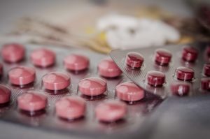 Close-up of pink round tablets in blister packs on a blurred surface.”] ,